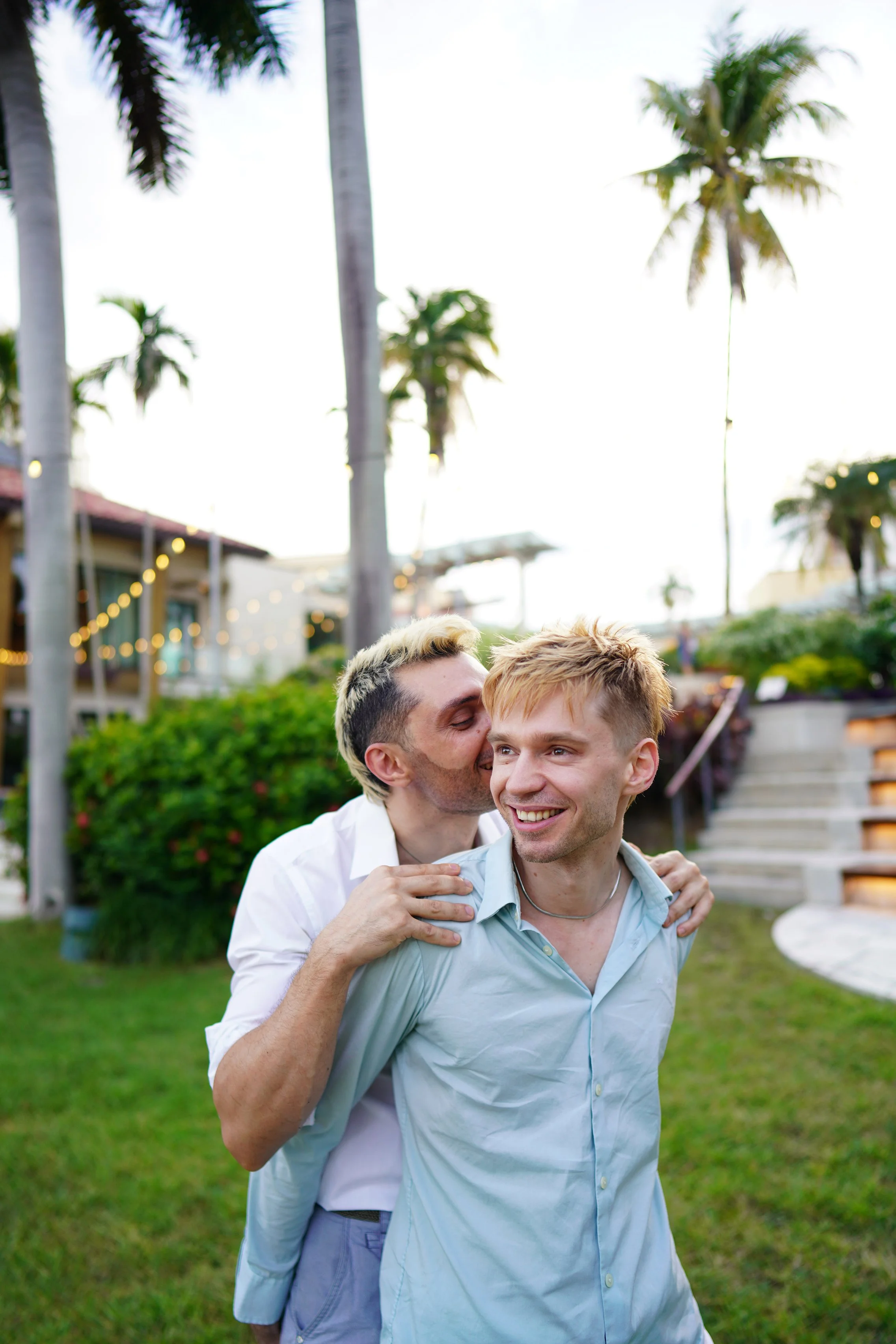 An intimate moment of a groom kissing his partner's ear under Florida palm trees, photographed by a San Francisco-based luxury wedding photographer.