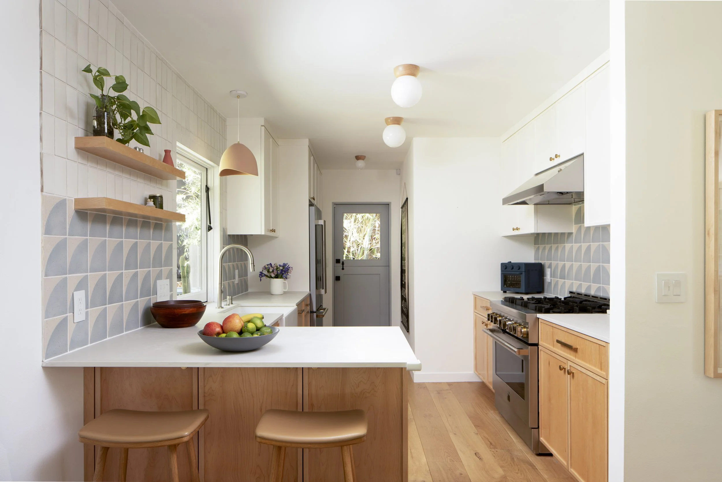 Kitchen with white cabinets, wooden lower cabinets, a gray door at the back, a stove, and a countertop with a bowl of apples and limes.