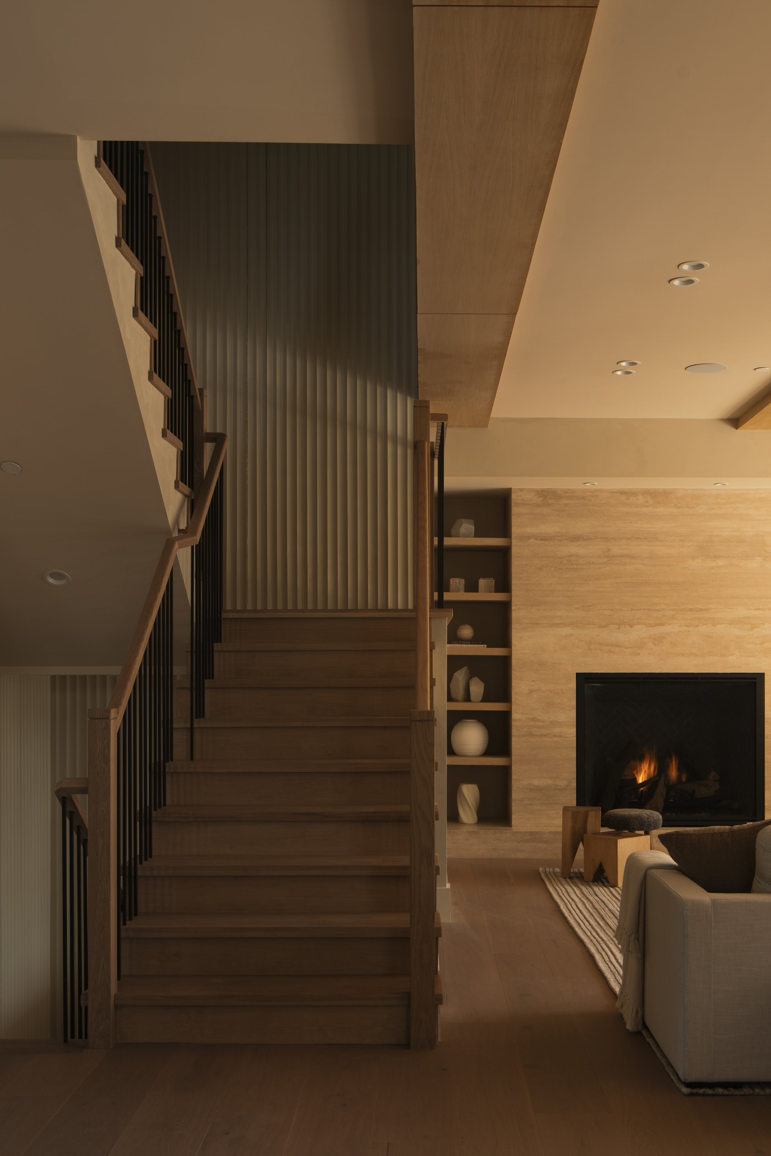 Interior of a modern living room with a staircase, fireplace, and shelf with decorative objects.
