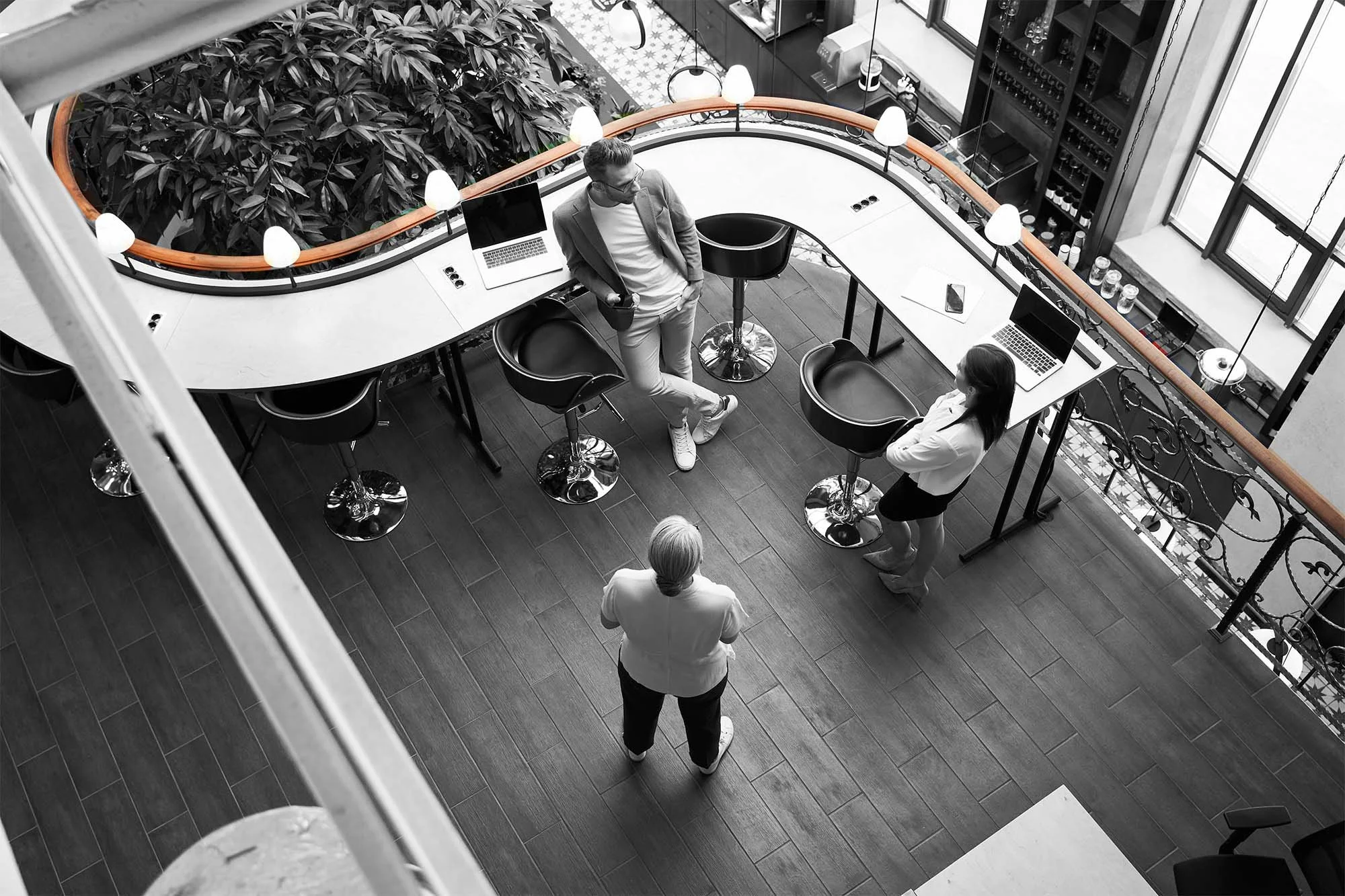 Overhead view of three business people in a modern office space with laptops on a curved desk, discussing and collaborating.