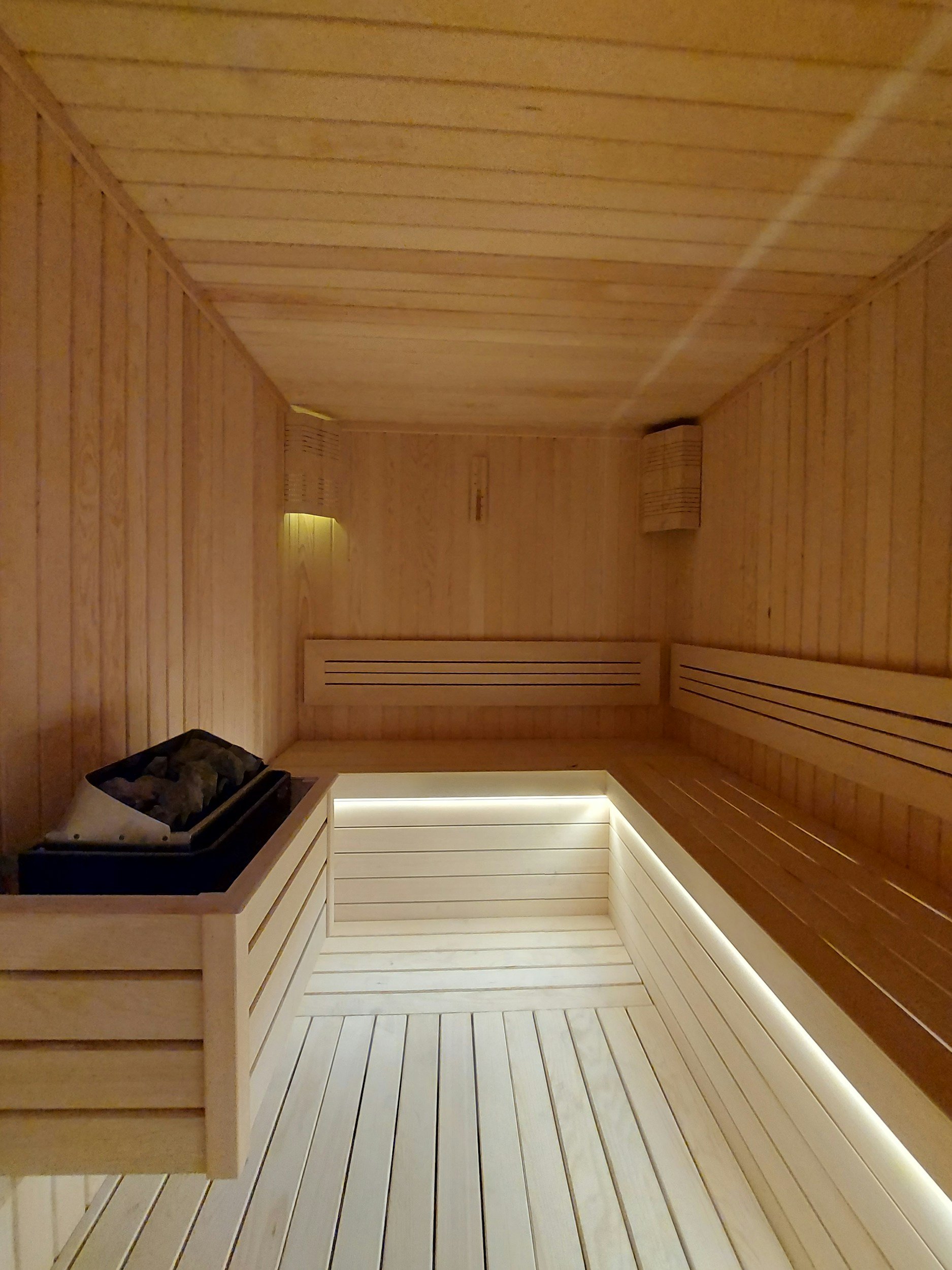 A wooden sauna with a heated rock stove, benches, and subtle lighting.