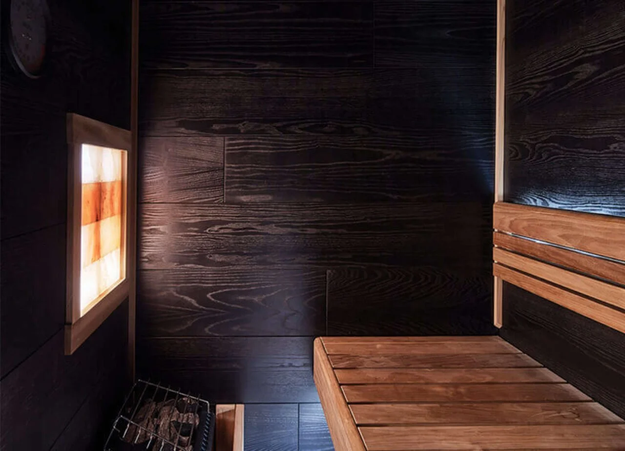 Interior of a sauna with dark wood walls and benches, and a lighted panel on the wall.
