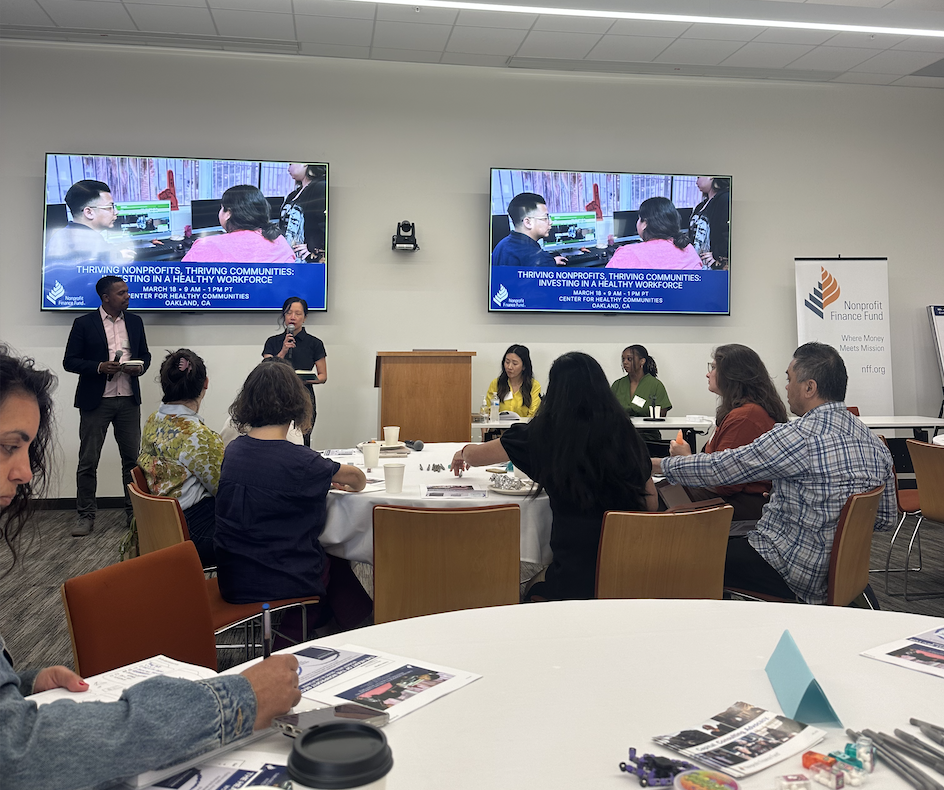 Nine people seated and standing in front of TVs showcasing research data about nonprofit wellbeing.