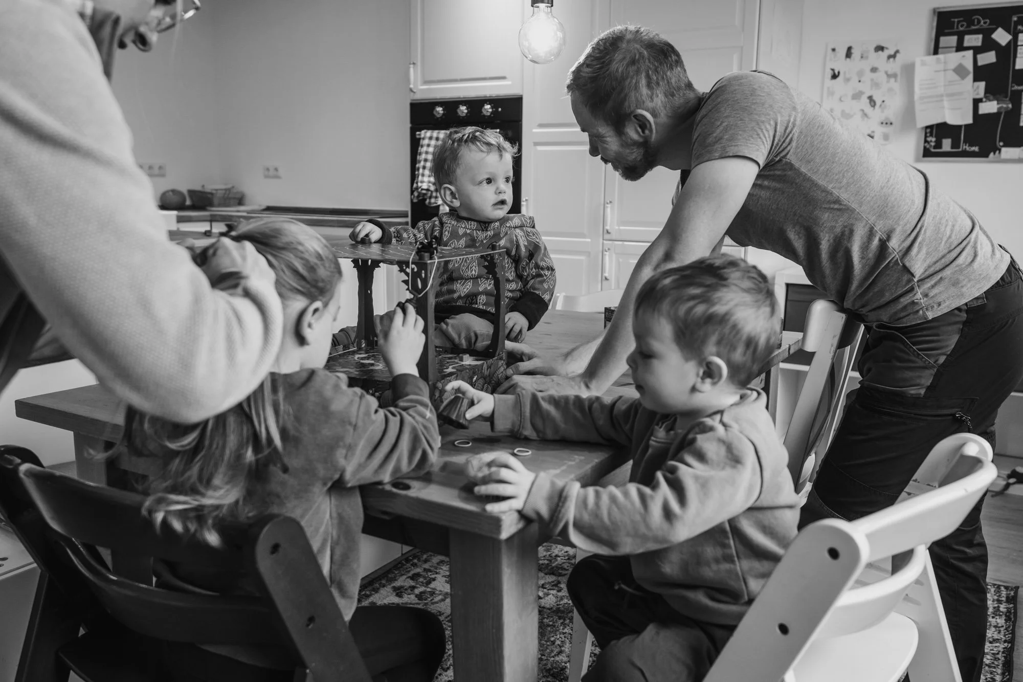 Kleinkind sitzt auf dem Esstisch, Mama flechtet Tochter die Haare