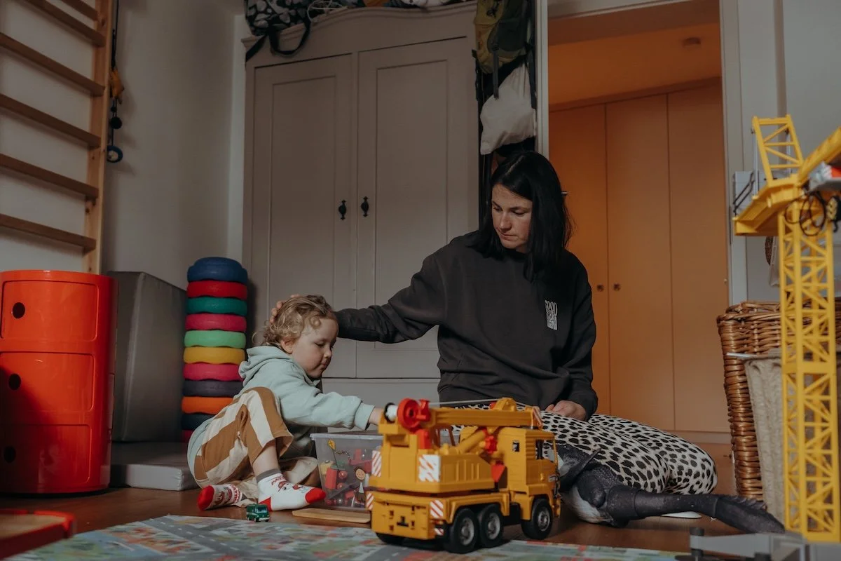 Eine Mama und ihr kleiner Sohn spielen im Kinderzimmer, dabei streichelt die Mama ihrem Kind liebevoll über den Kopf.