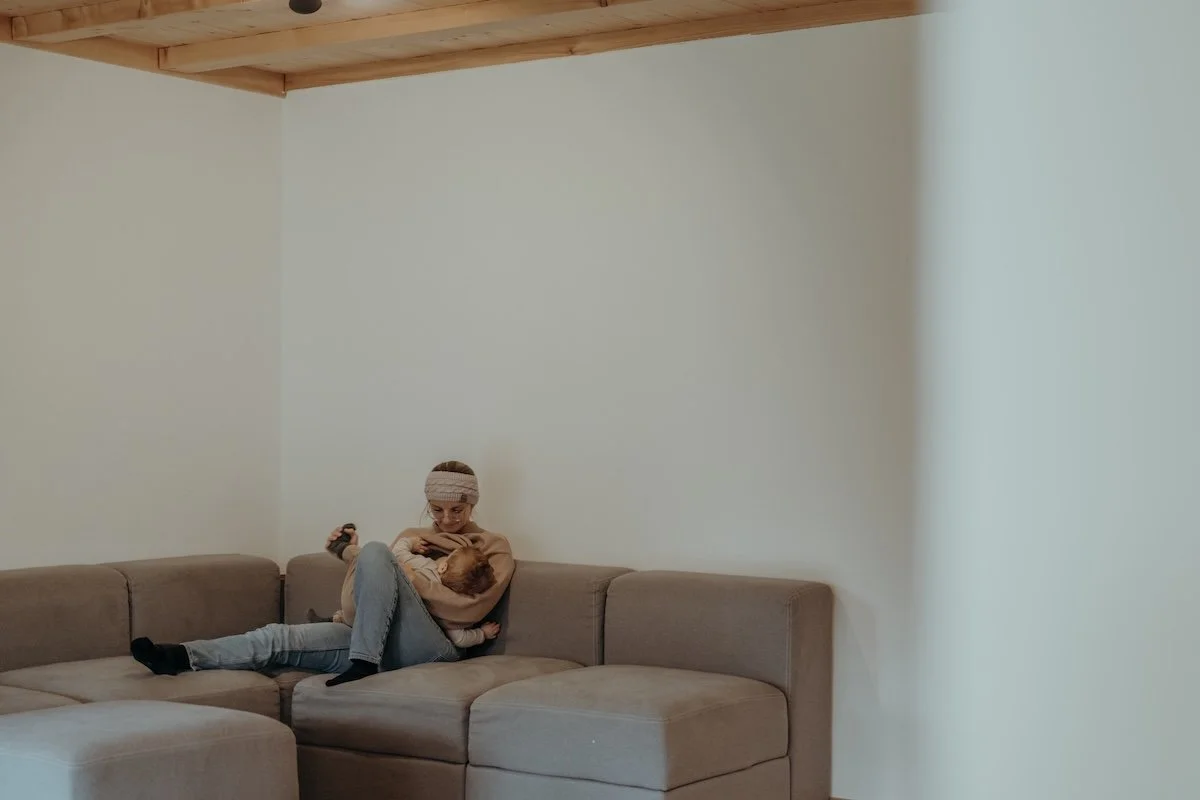 Eine Mama stillt ihr Kleinkind auf dem Sofa im Wohnzimmer.