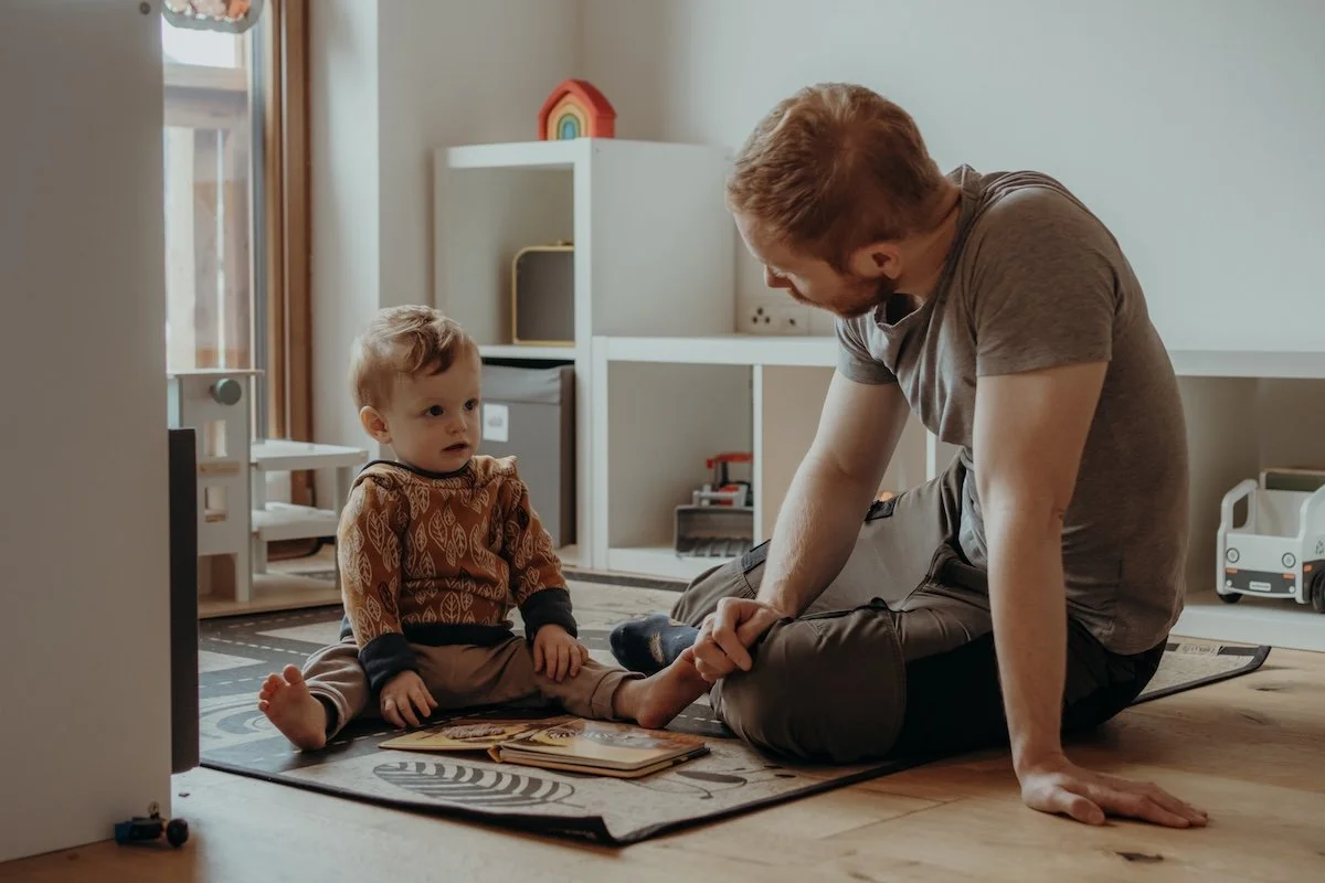 Der Papa spielt mit seinem kleinen Sohn im Kinderzimmer auf dem Boden, die beiden sehen sich dabei liebevoll an.