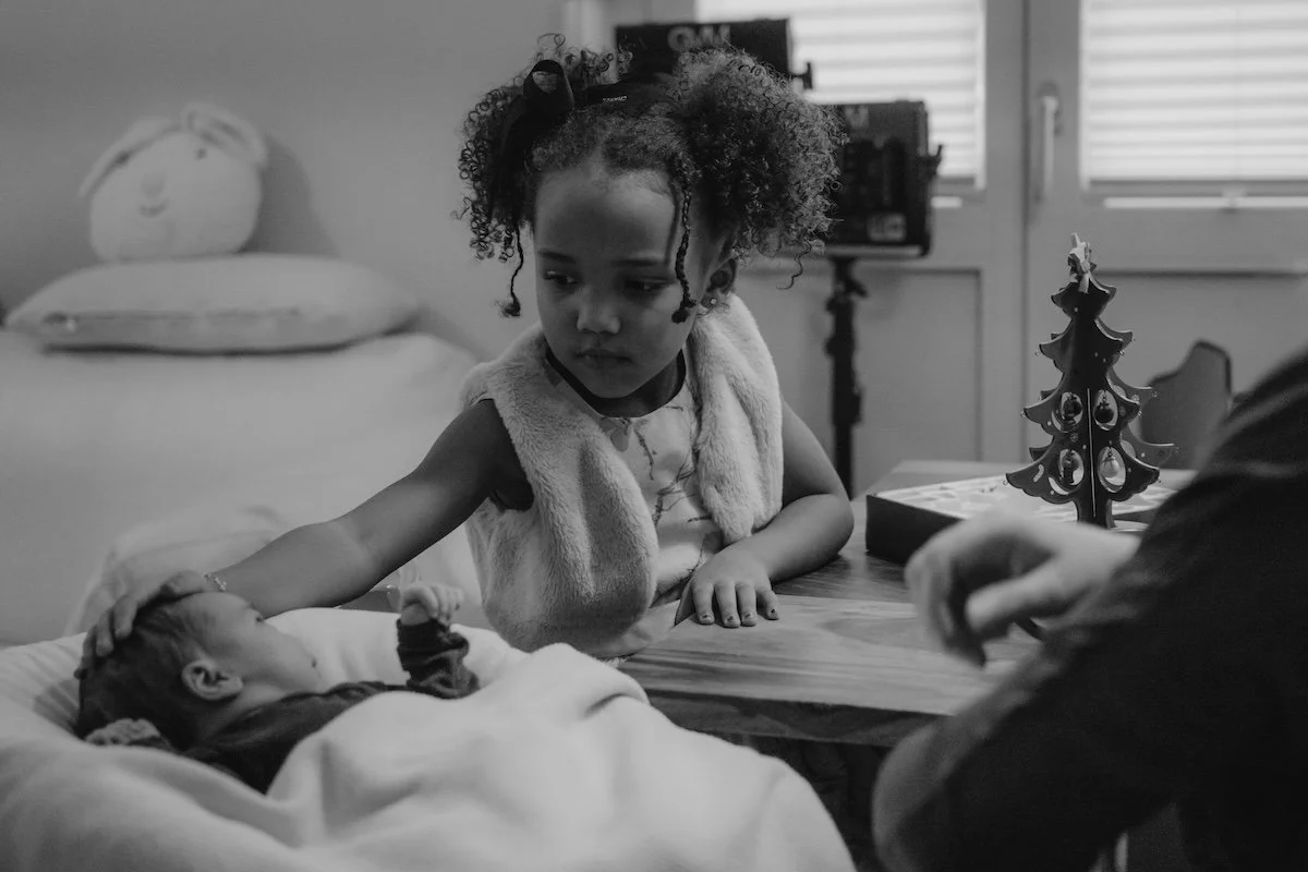 Die ältere Schwester schieht ihre kleine neugeborene Schwester liebevoll an und streichelt ihr sanft über den Kopf.