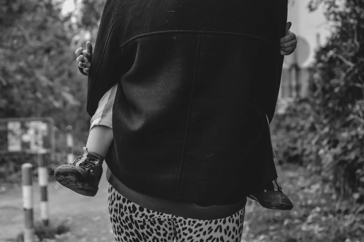 Eine Mama trägt ihren kleinen Sohn vor dem Bauch im Arm. 