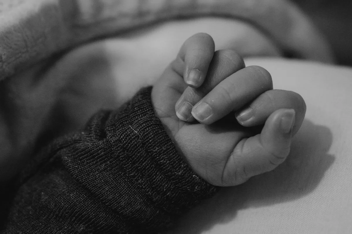 Nahaufnahme von der Hand mit zarten Fingern und kleinen Fingernägeln eines Neugeborenen.