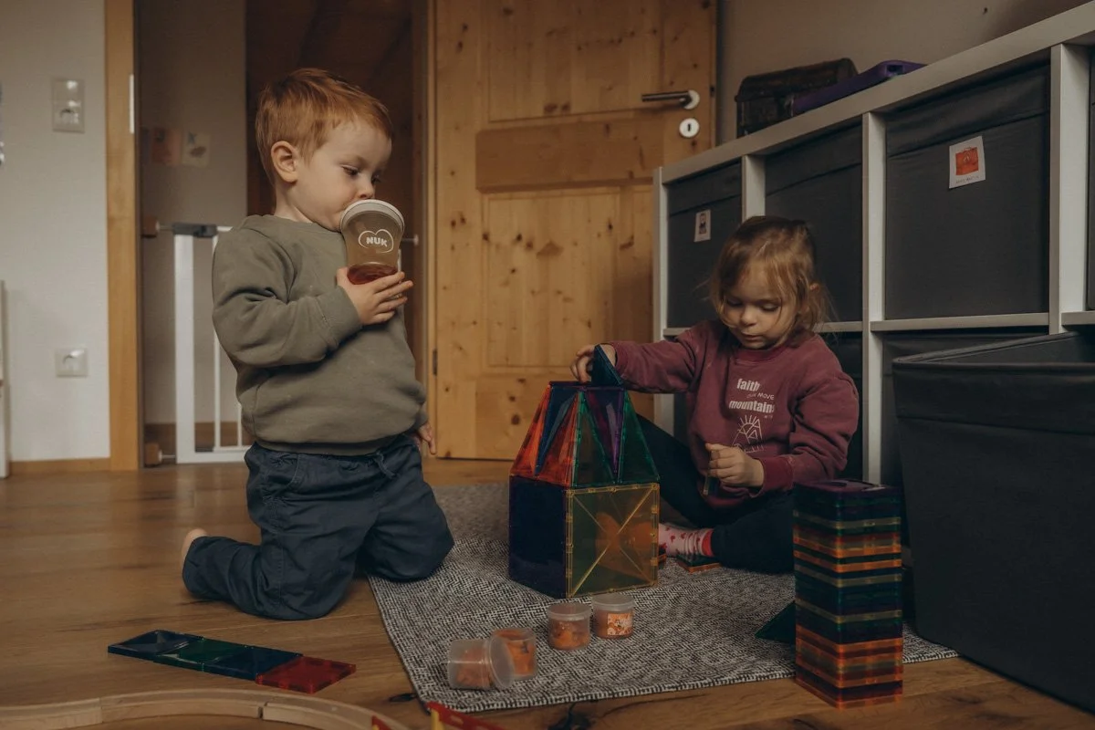 Spielzeug oder Kleidung mieten als Geschenkidee zur Geburt, über die sich jede Mama freuen wird. Zwei Kinder spielen im Kinderzimmer mit Magnetbausteinen