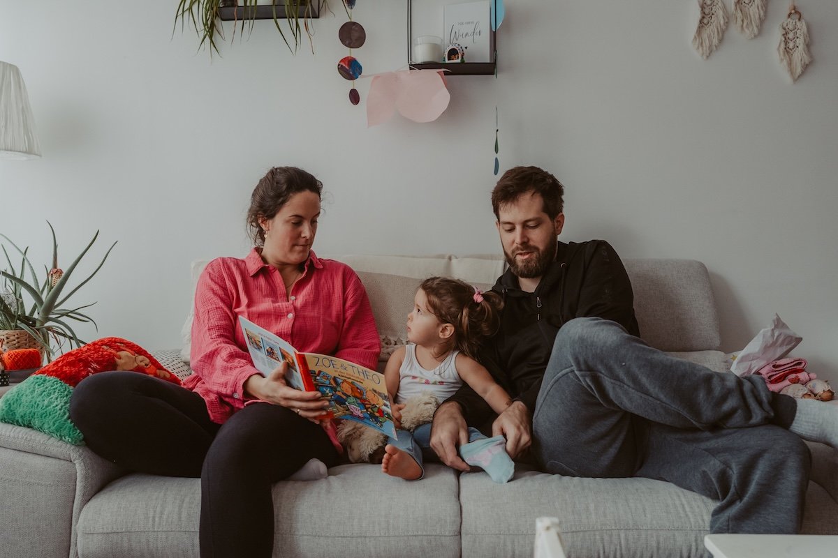 Eltern sitzen mit Tochter auf dem Sofa und schauen Buch an