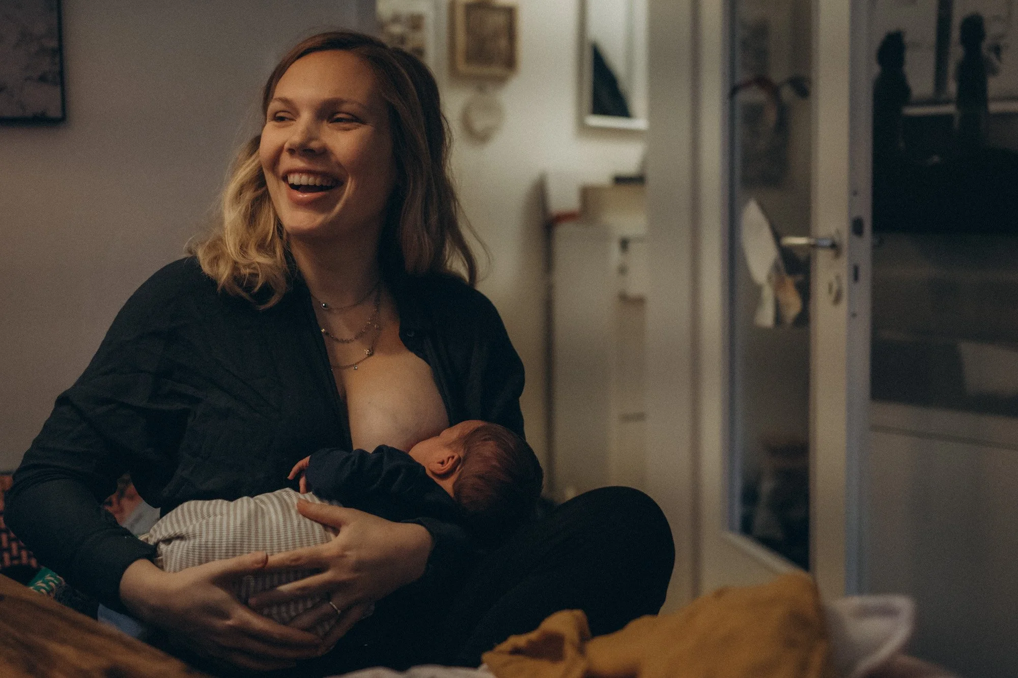 5 Geschenkideen zur Geburt, über die sich jede Mama freuen wird. Lächelnde aber müde Mama mit stillendem Baby im Arm im Wochenbett