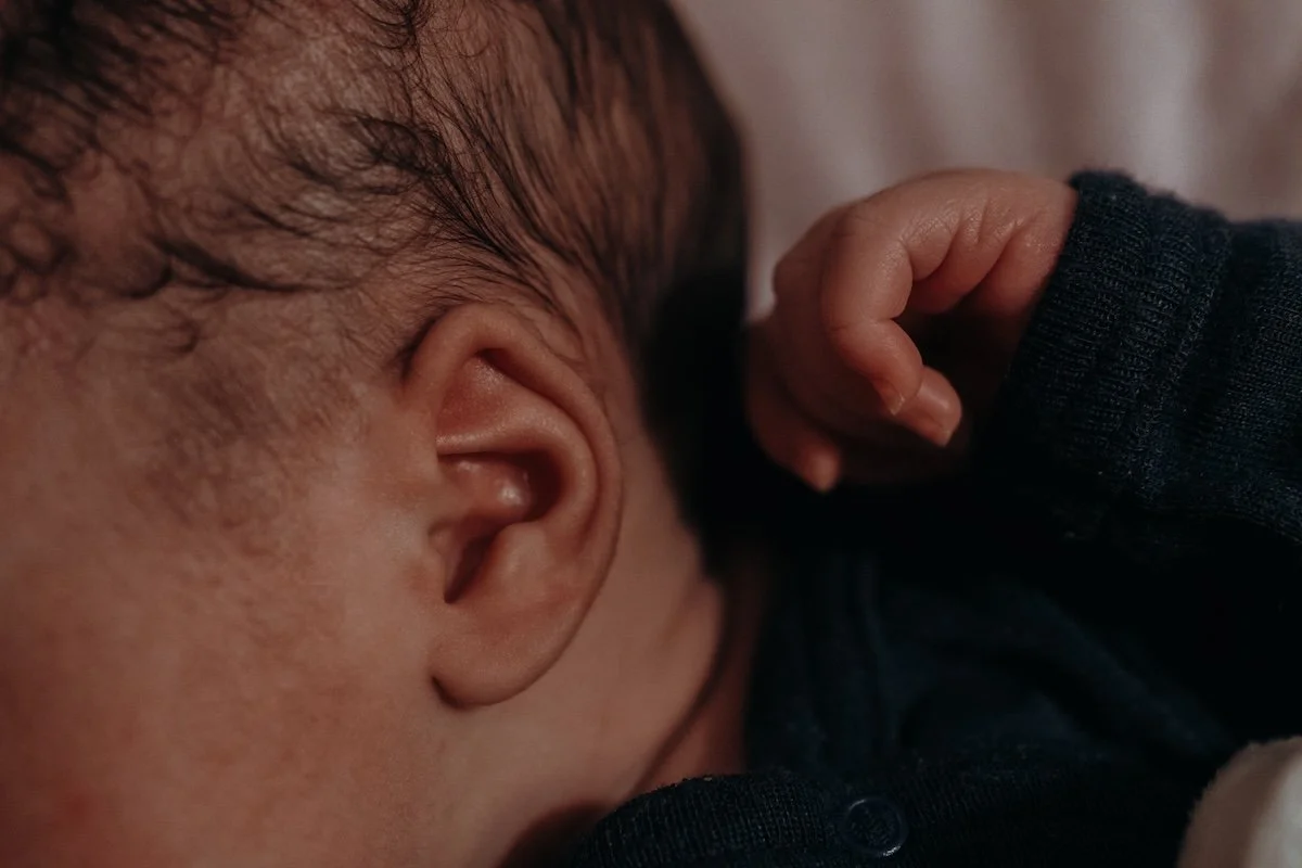 Nahaufnahme vom zarten Flaum auf dem Kopf und am Ohr und der kleinen Hand eines neugeborenen Babys.