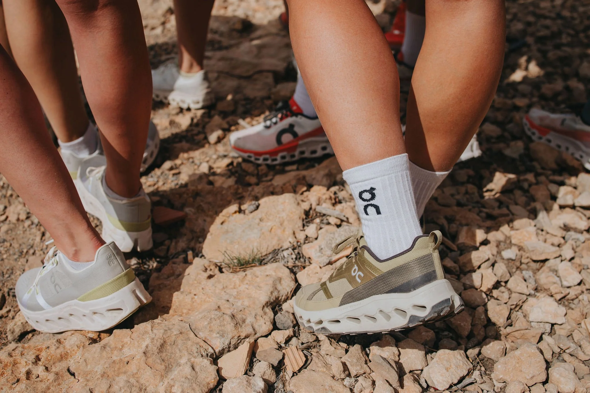 Group of people wearing athletic shoes, standing on rocky terrain.
