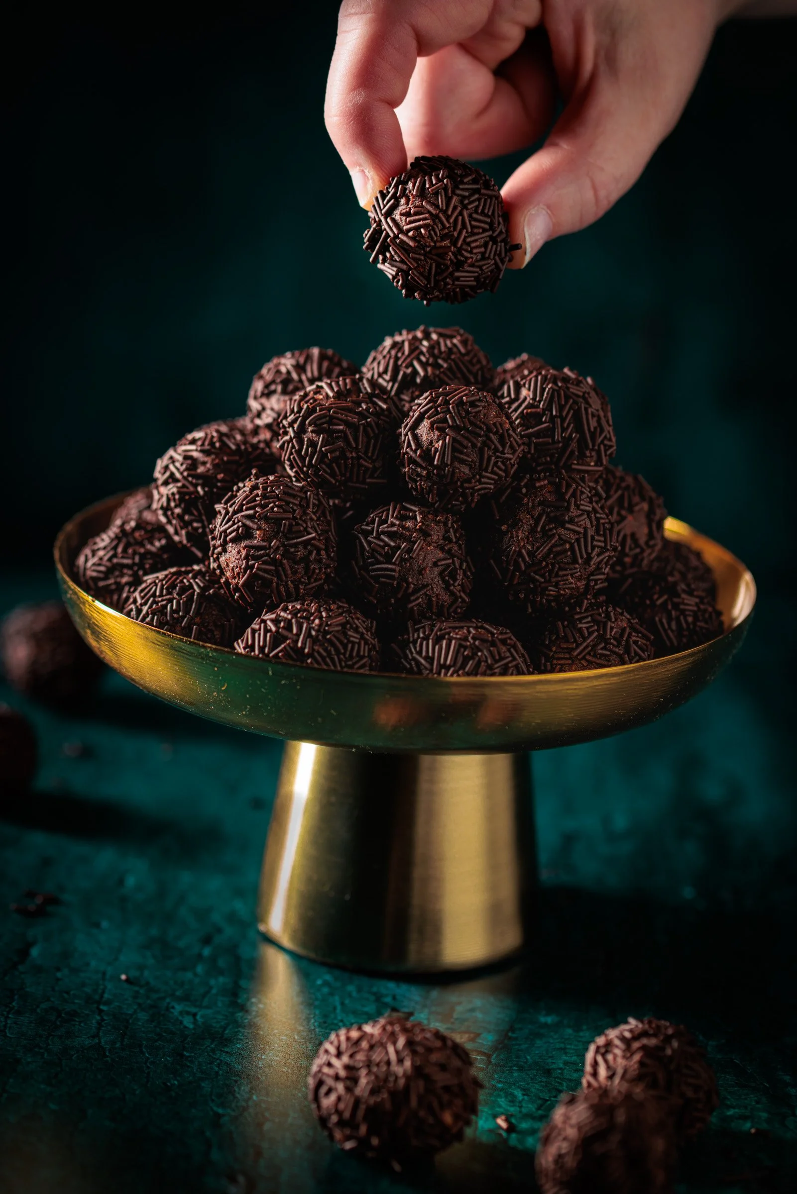 Schüssel voller Schokoladentrüffel mit Schokoladenstreuseln, eine Hand platziert einen Schokoladentrüffel auf die schon stapelnden Trüffel.