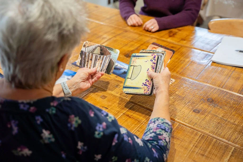 Person with gray hair looking at a deck of cards with nature themed images on a wooden table.