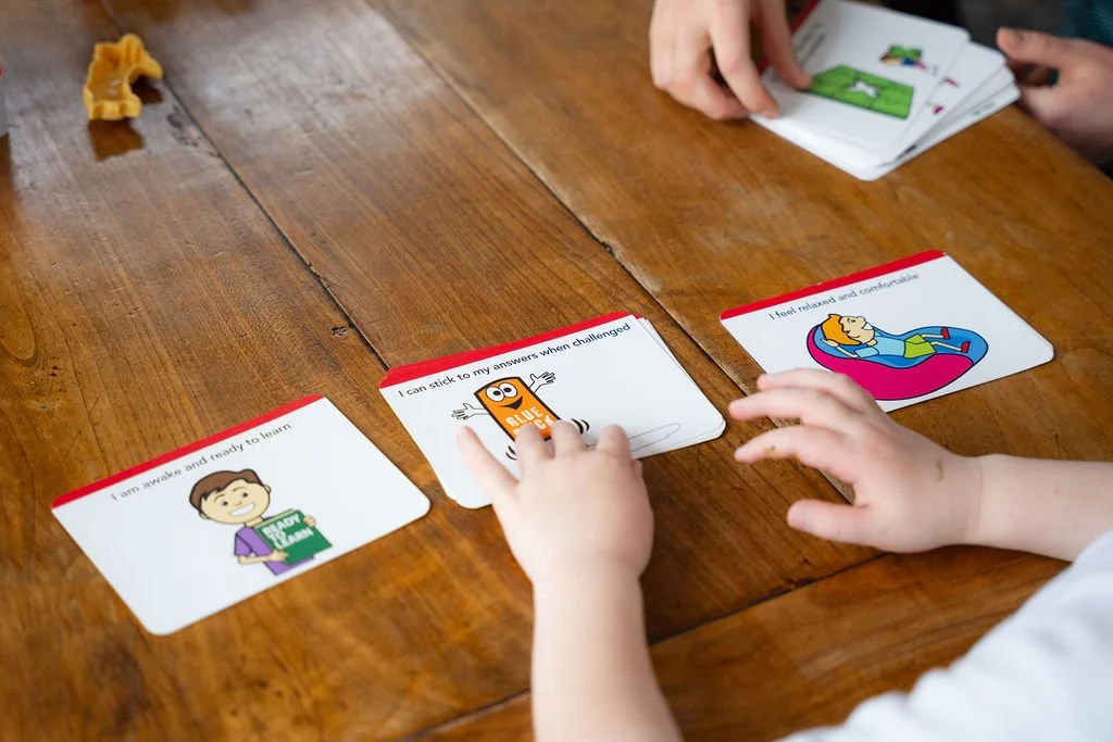 A child looking at and sorting cards with pictures and short phrases about learning on a wooden table.