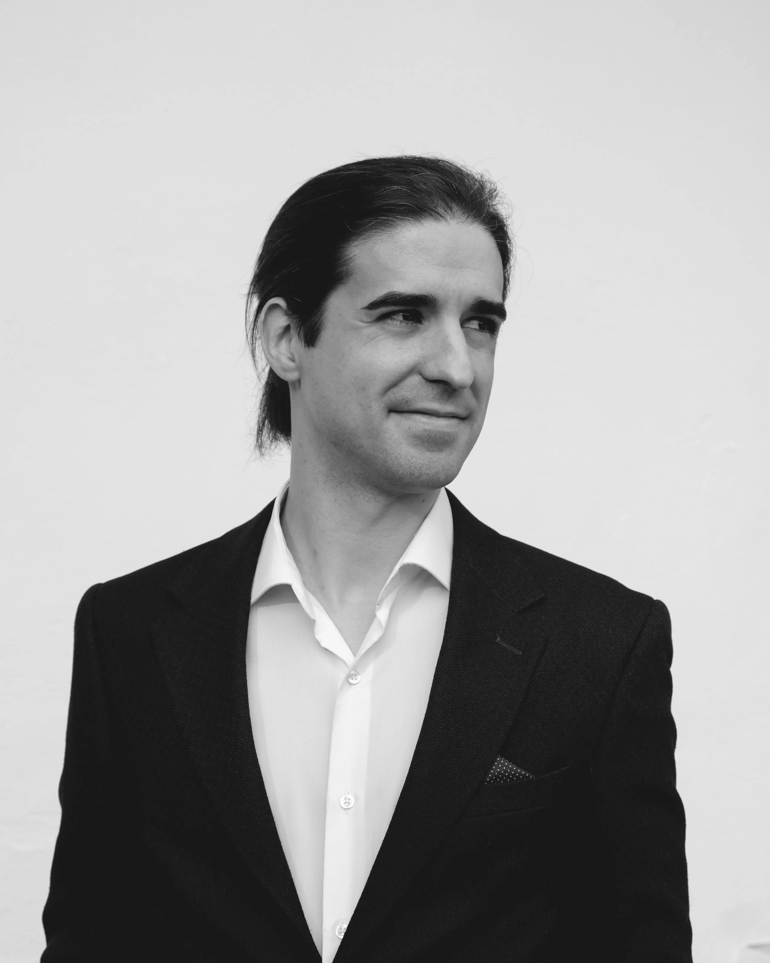 A man in a blue suit and tie with arms crossed, smiling confidently against a white background.