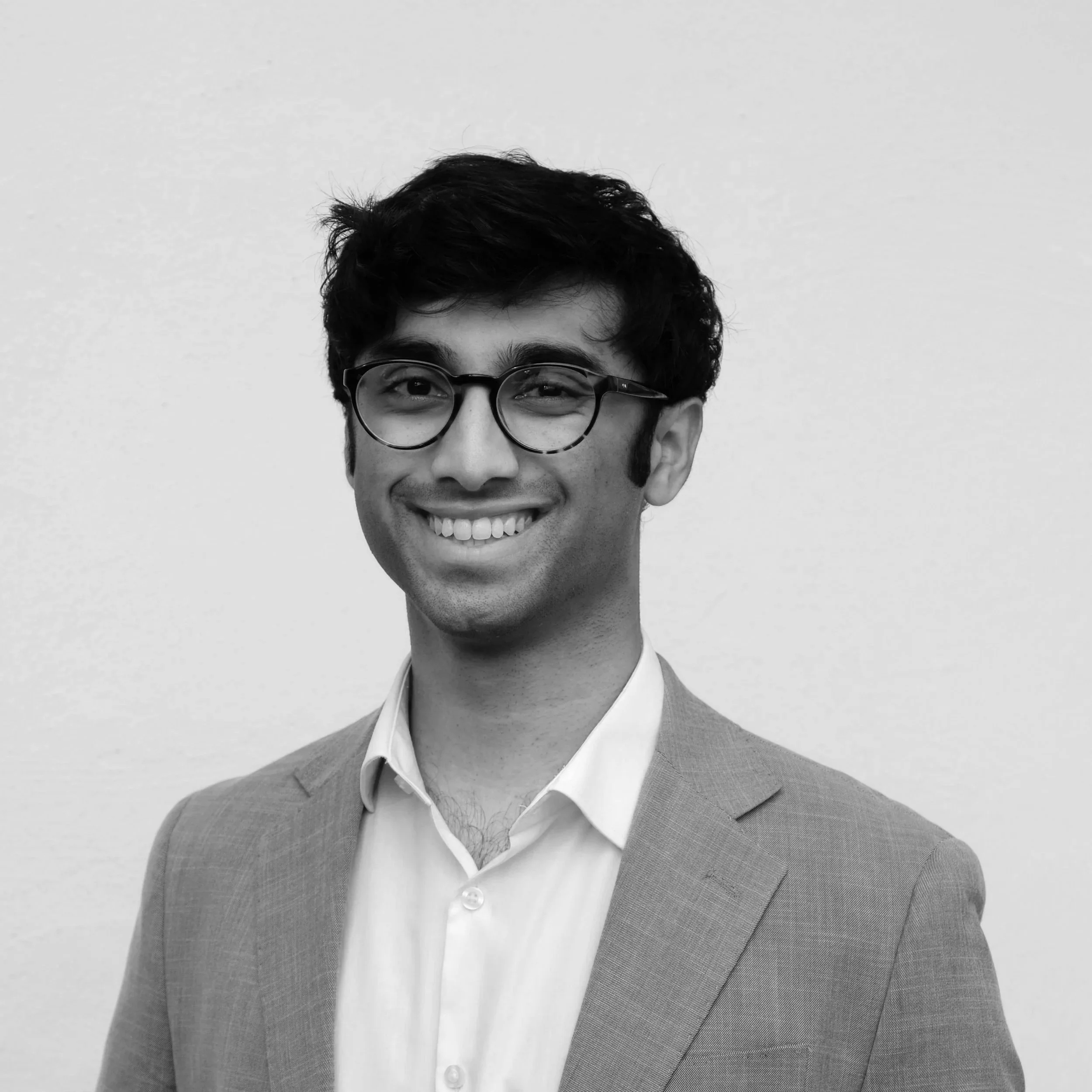 Smiling young man with black hair, glasses, and a maroon t-shirt against a white background.