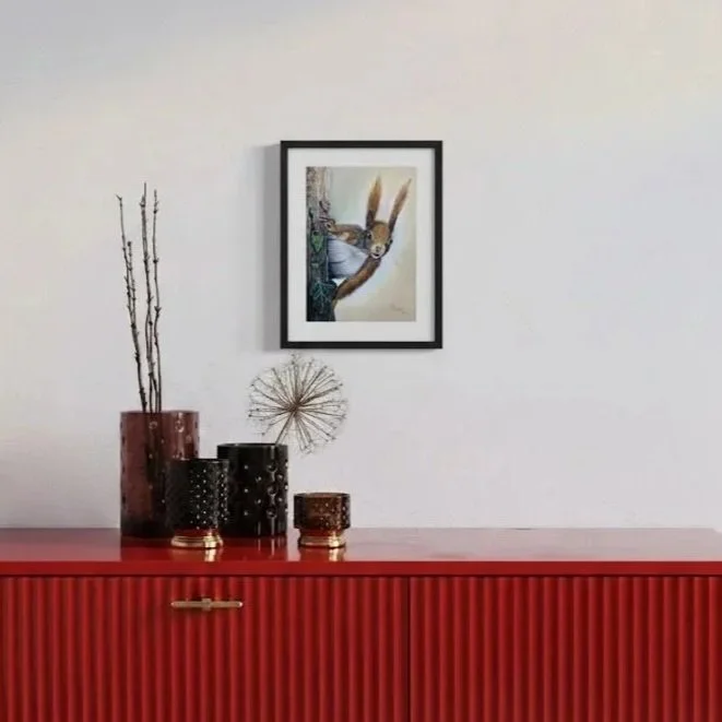 Ein roter Sideboard mit Dekogefäßen, einer stilisierten Drachenfigur und einem Kunstbild auf der Wand darüber.