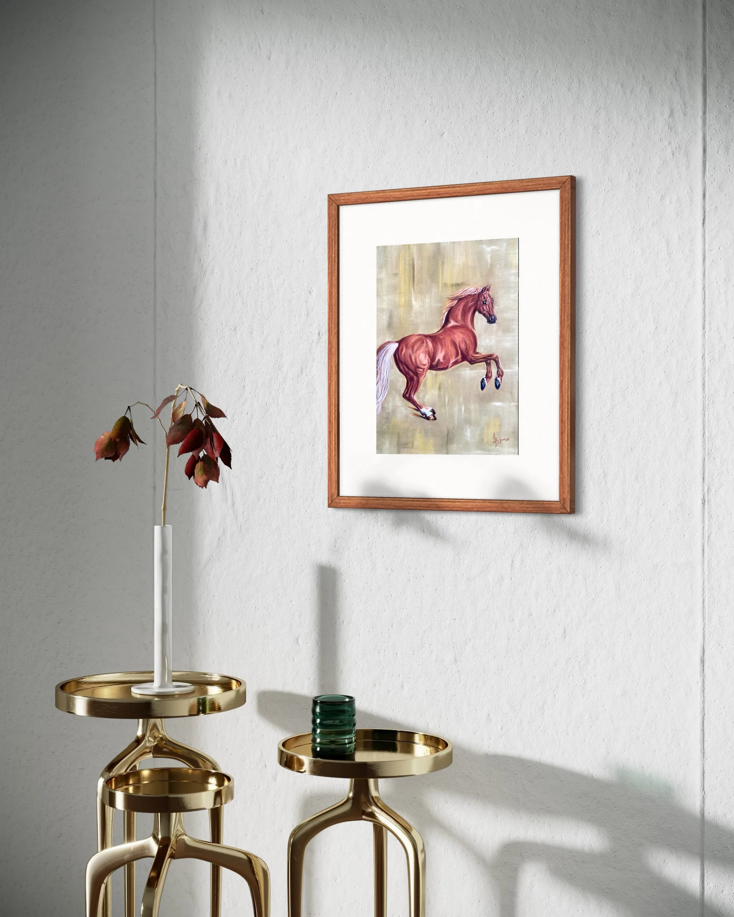 Ein gerahmtes Bild eines galoppierenden braunen Pferdes hängt an einer weißen Wand. Vor der Wand stehen zwei goldene Beistelltische, der eine mit einer weißen Vase und einem Zweig mit roten Blättern, der andere mit einem grünen Glas.