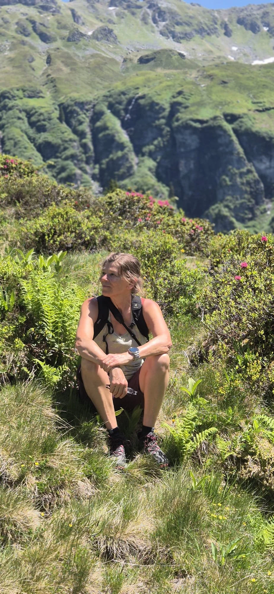 Christa sitzt an einem Hang in den Bergen inmitten von Alpenrosen