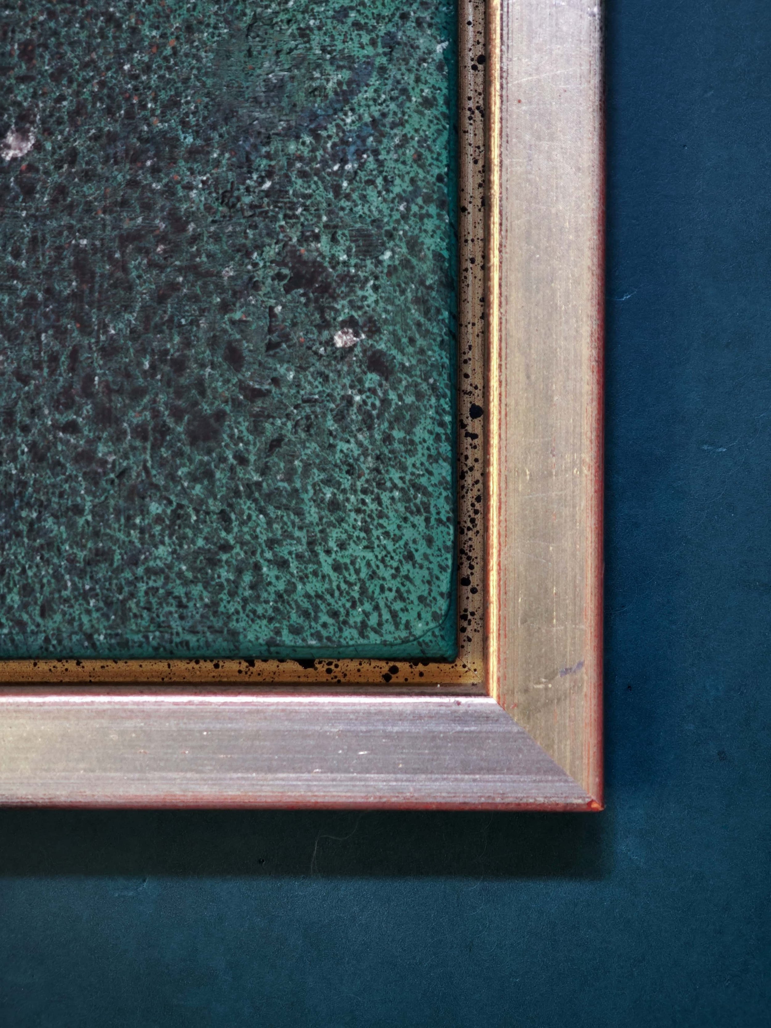 Nahaufnahme eines quadratischen Kunstwerks mit einem grünen, texturierten Feld, umrahmt von einem messingfarbenen Rahmen und einem blauen Hintergrund.