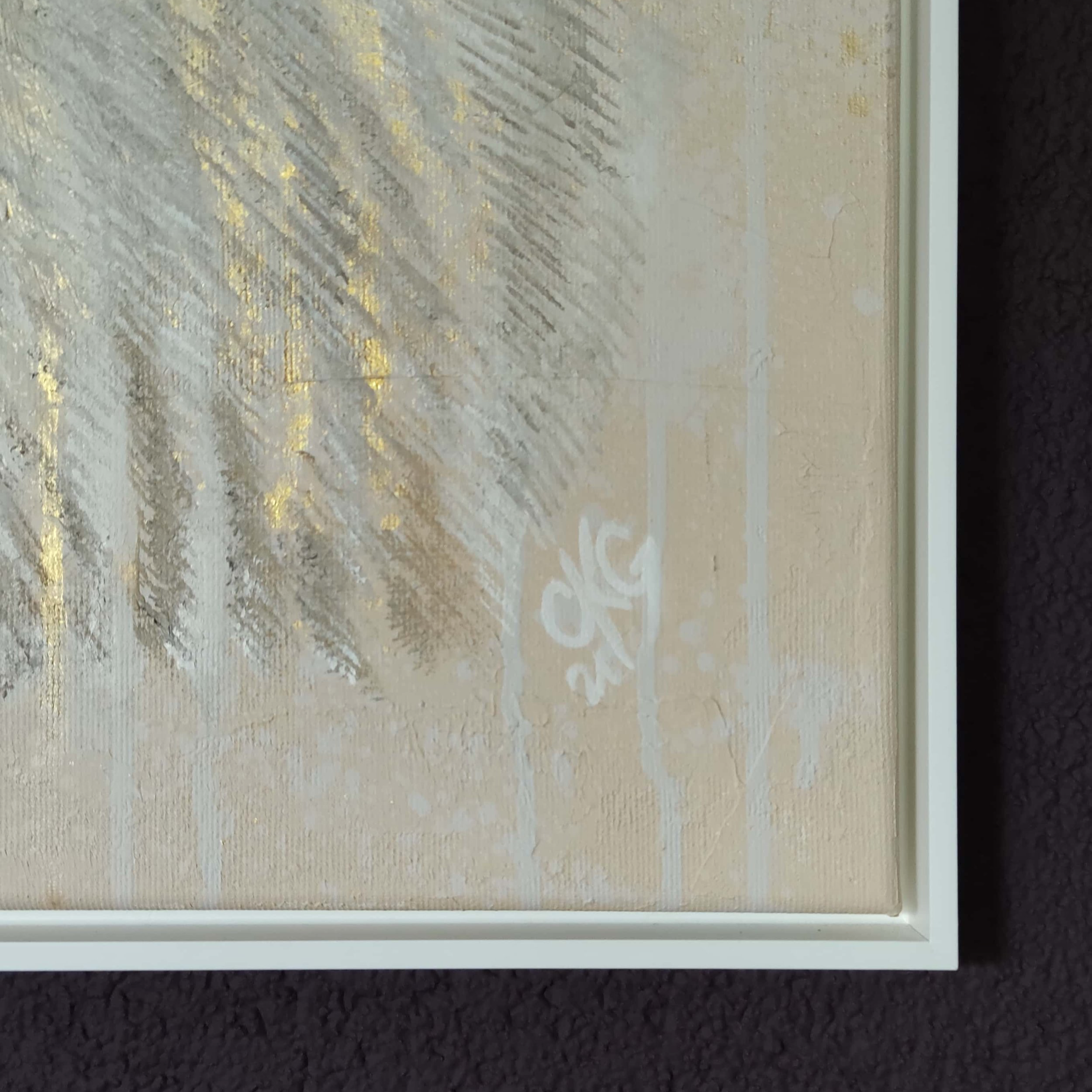 Details eines abstrakten Gemäldes mit goldenen Akzenten auf einer hellen, strukturierten Oberfläche in einem weißen Rahmen.