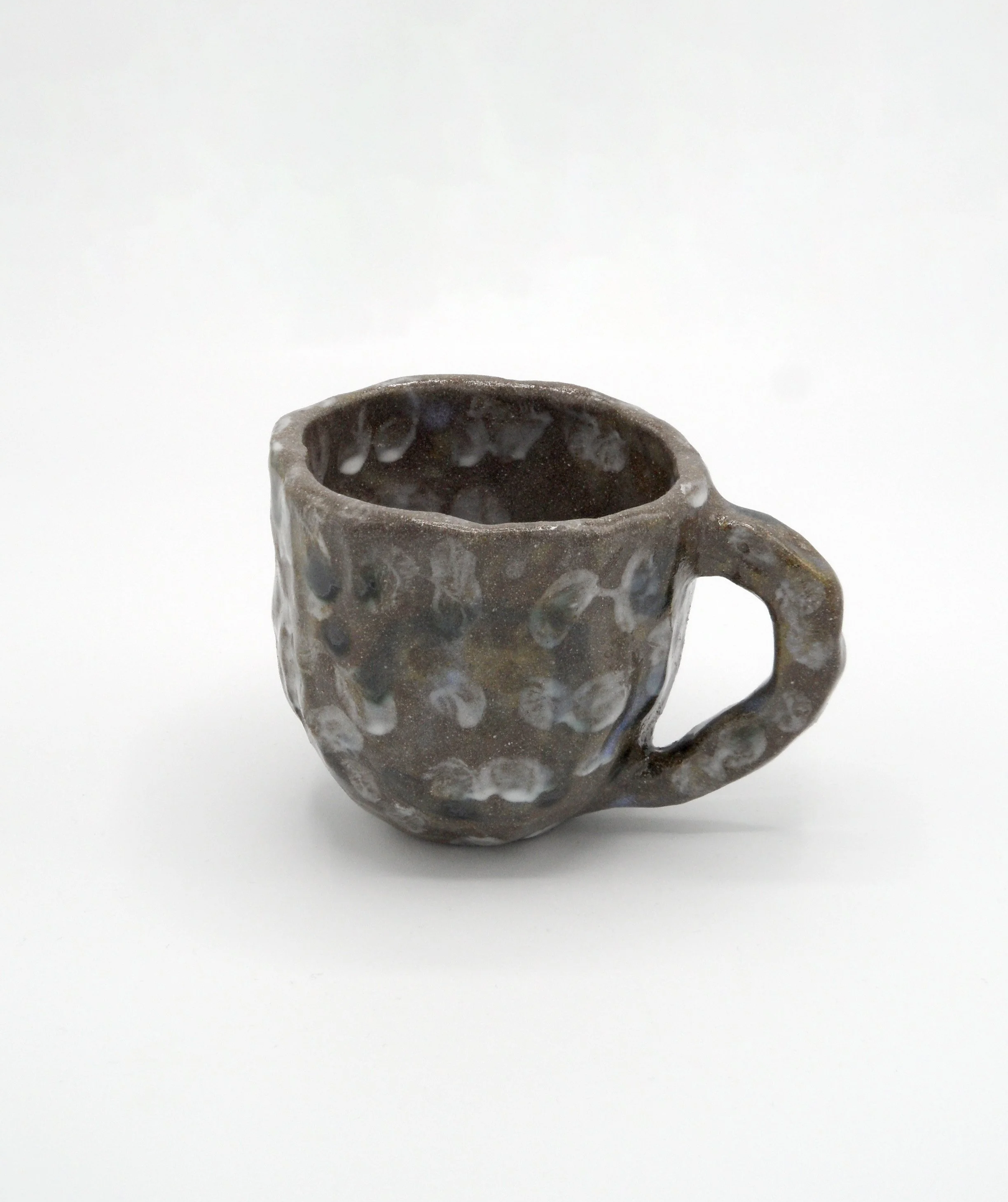 Tasse en céramique avec une surface texturée, vue du dessus, sur fond blanc. Pièce unique produite par Chloé Hercé, en modelage.