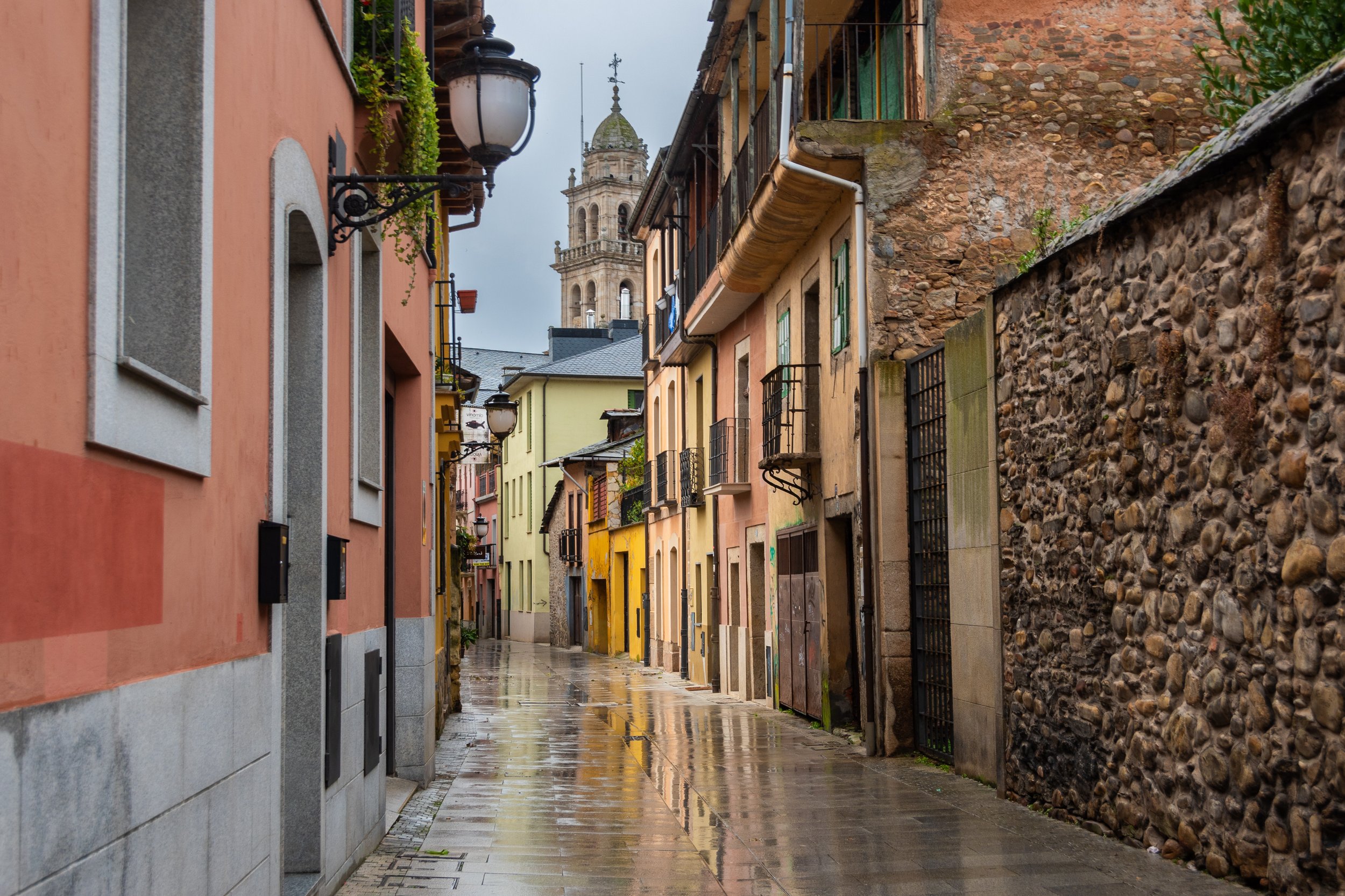 Calles estrechas con edificios de colores pastel y una torre de iglesia visible al fondo, después de la lluvia.