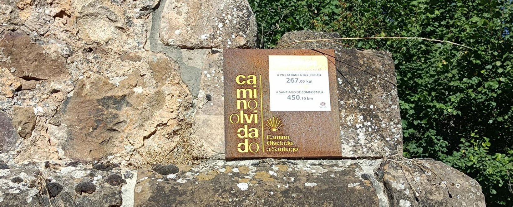 Placa en piedra que indica kilómetros a Villaranca del Bierzo y Santiago de Compostela, parte del Camino Olvidado a Santiago.