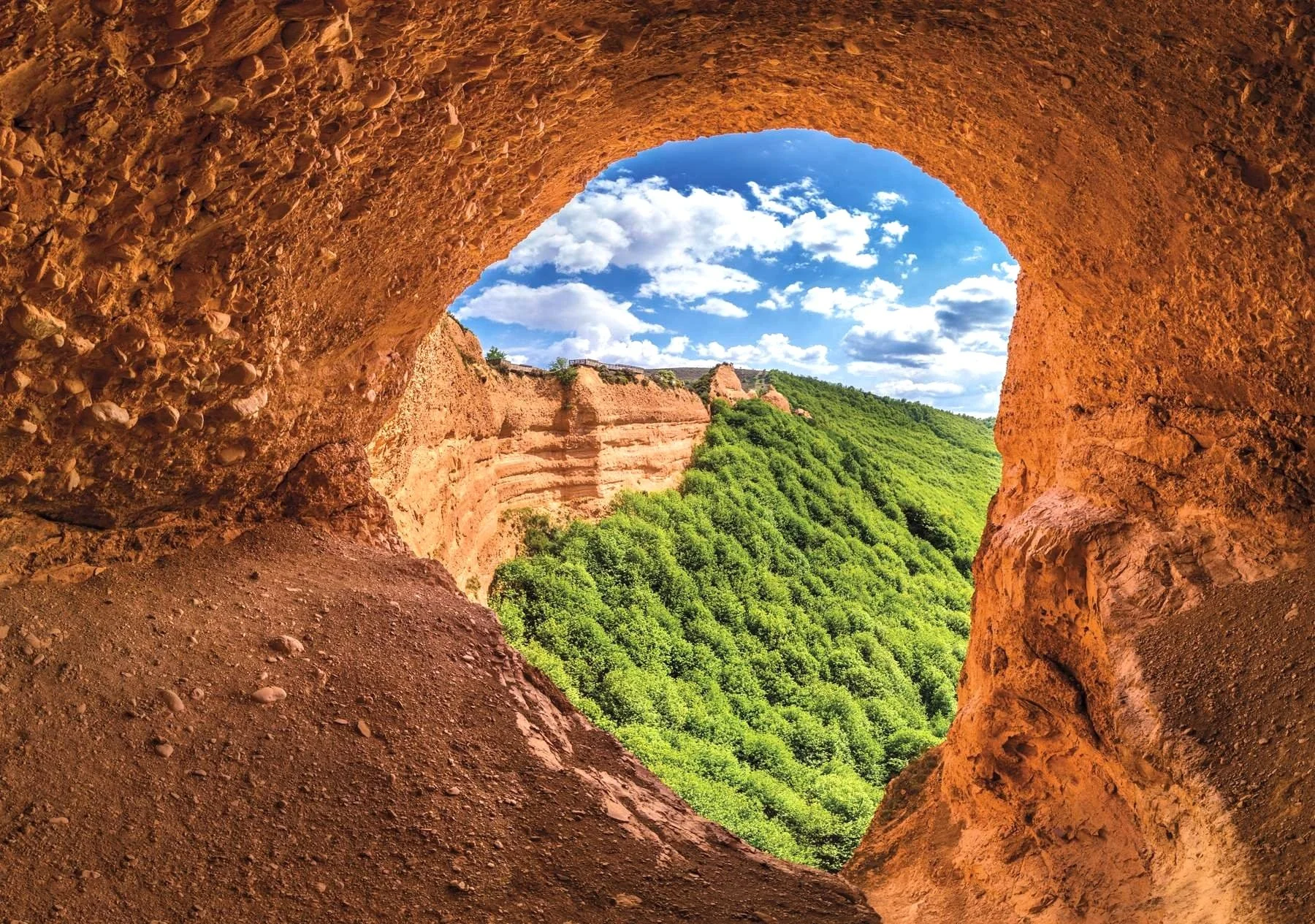 Vista desde la cueva de las médulas, mostrando colinas con vegetación y un cielo azul con nubes.