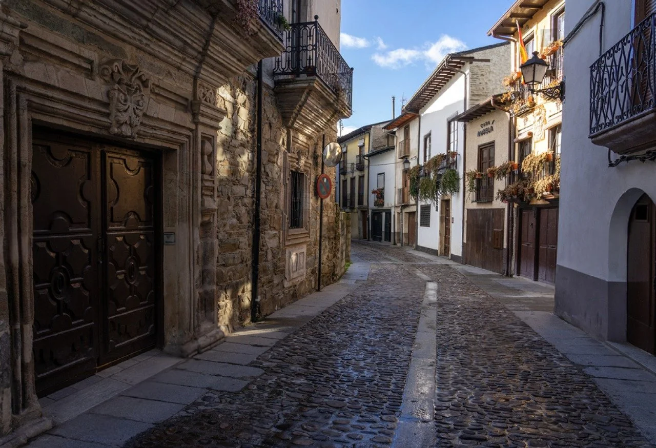 Calles empedradas en un pueblo con casas de fachadas blancas y balcones con flores, en un día soleado.
