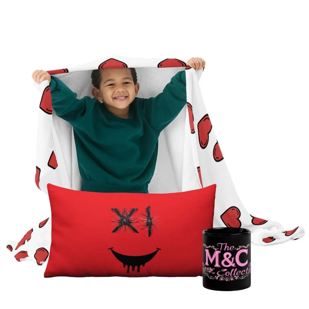 A smiling young boy holding a white blanket with red hearts. In front of him is a red pillow with a smiling face, 'X' for eyes, and a black dripping smile. To the right is a black container with pink text that reads 'The M&C Collection.'