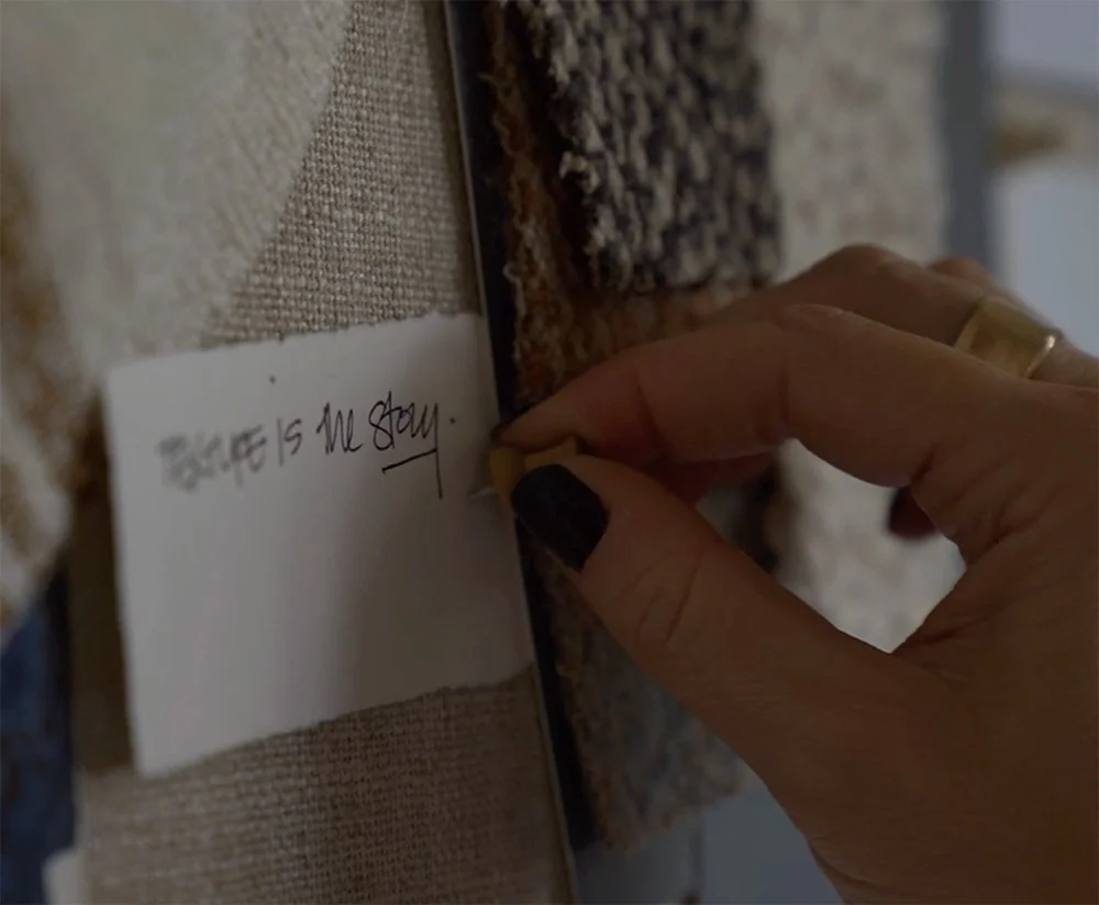 A person is writing on a small white card pinned to a fabric-covered board with textured fabric squares.