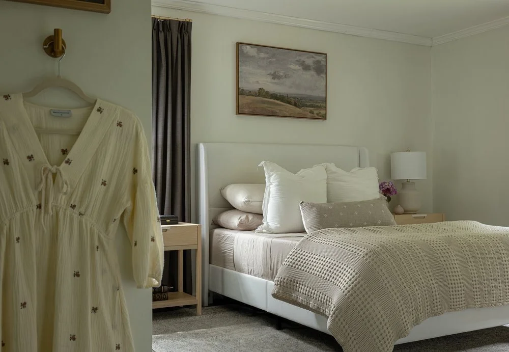 Neutral, modern bedroom with bed, wall hooks, and wooden wide tables