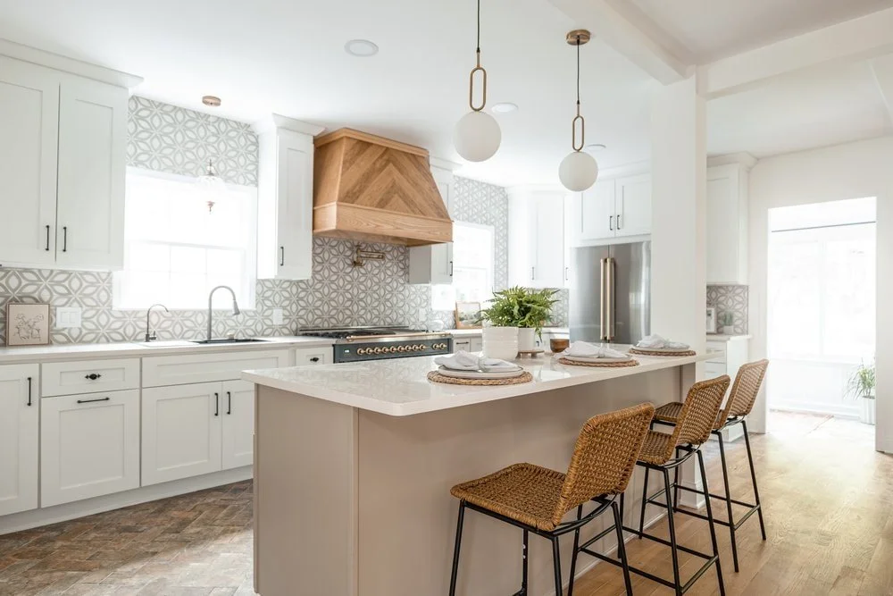 Luxury kitchen design in Georgia with a herringbone custom range hood, brick textured floors, milk glass pendant lighting, and white kitchen cabinetry.