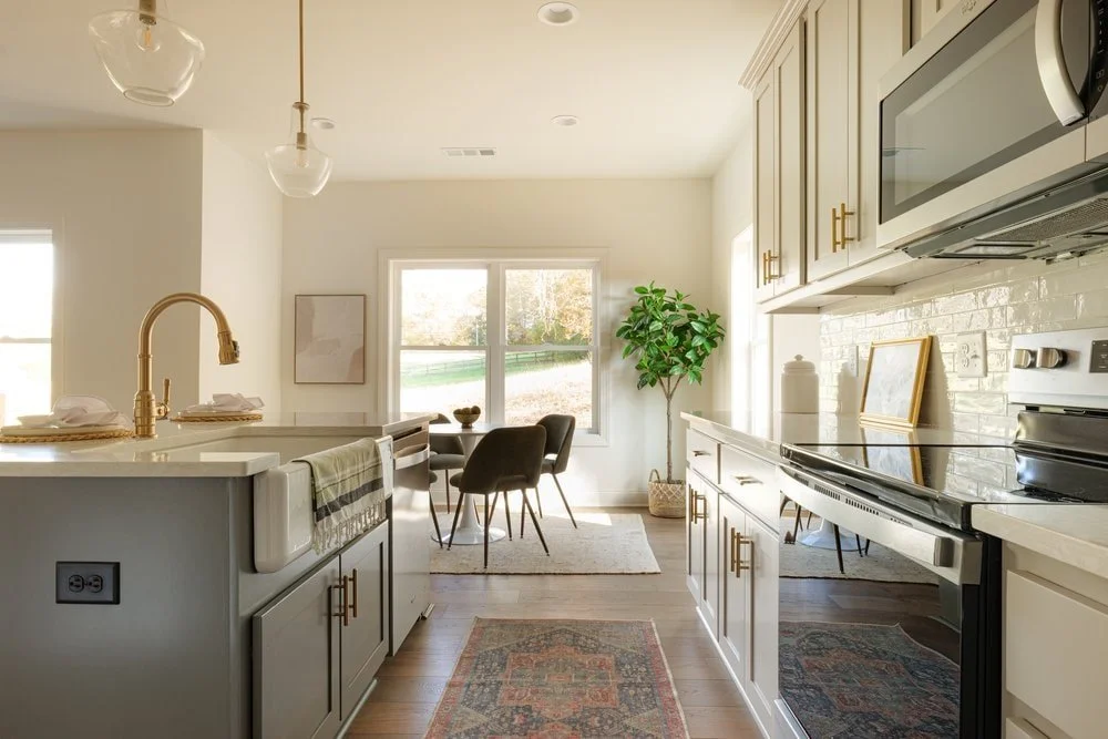 Side view of custom kitchen with two toned cabinetry and traditional runner rug with breakfast nook and oversized windows in background.