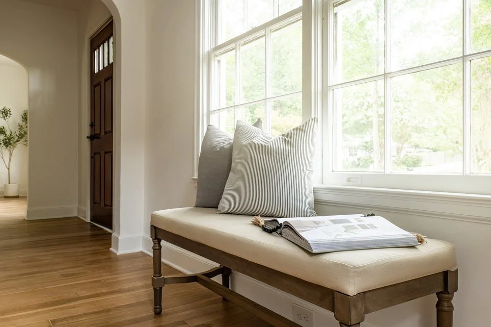 Side detail in Georgia home with walnut stained traditional front door and arched walkways in background, Bench and pillows under large window in focus