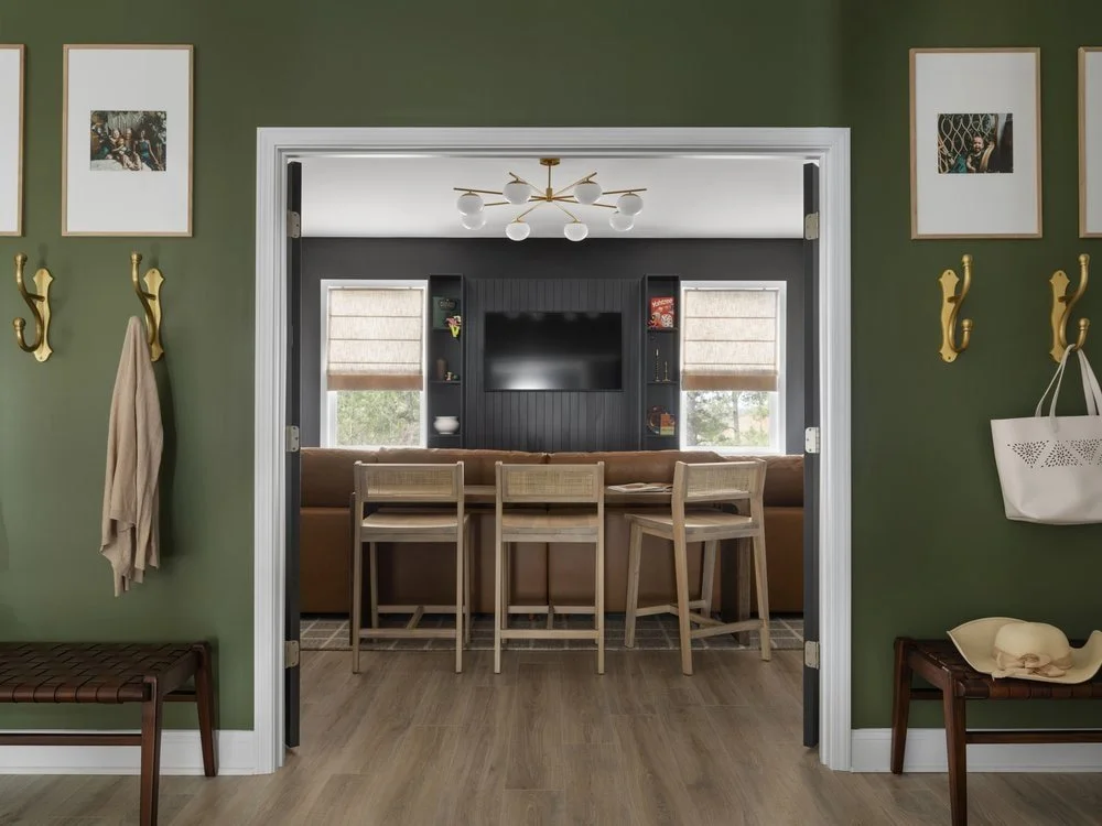 Full view of media room upstairs on second level with leather benches and oversized wall hooks for a mudroom design. View of the interior media room with leather sofa, TV, and black custom cabinetry.