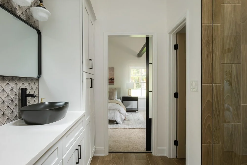 Full bathroom remodel view with sliding glass door, white custom cabinetry storage and wood flooring.