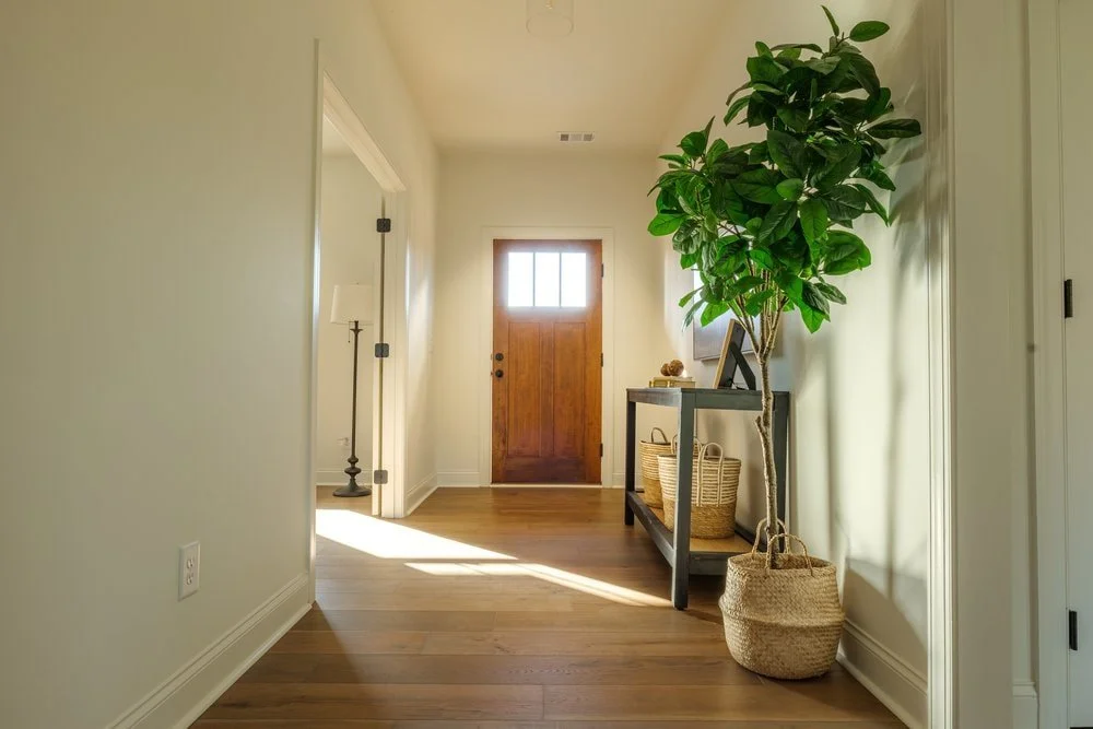Simple entryway with walnut stained door and clean white walls adjacent to home office to the left.