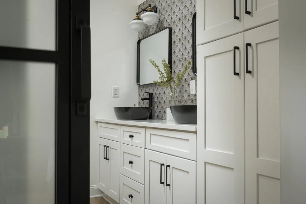 Modern bathroom renovation with patterned backsplash, black accent mirrors and custom white cabinetry for storage.