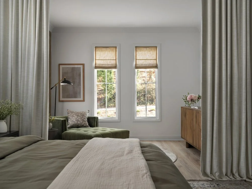 Sitting area in master bedroom with floor to ceiling curtain divider and a velvet chaise with linen roman shades over the windows.