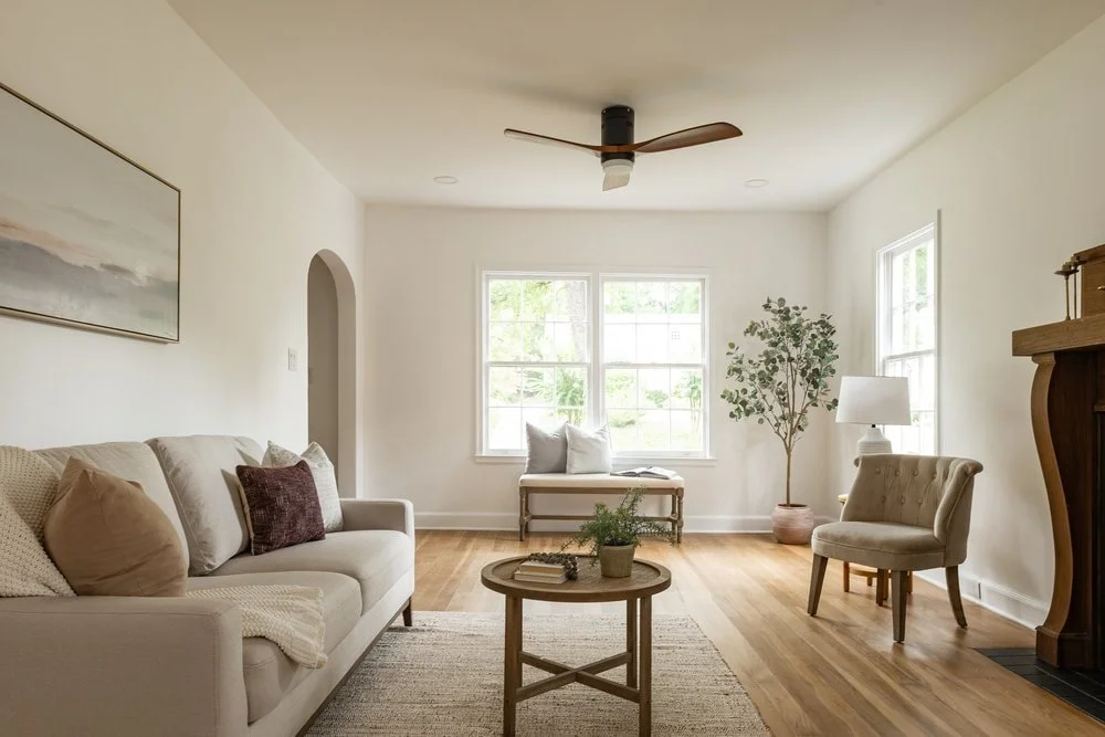 Full living room view in Georgia home renovation with original walnut fireplace, white sofa, round coffee table and honey oak flooring.