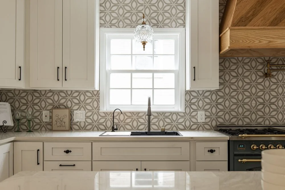Luxury kitchen design in Georgia with a herringbone custom range hood, traditional glass pendant lighting, and geometric backsplash