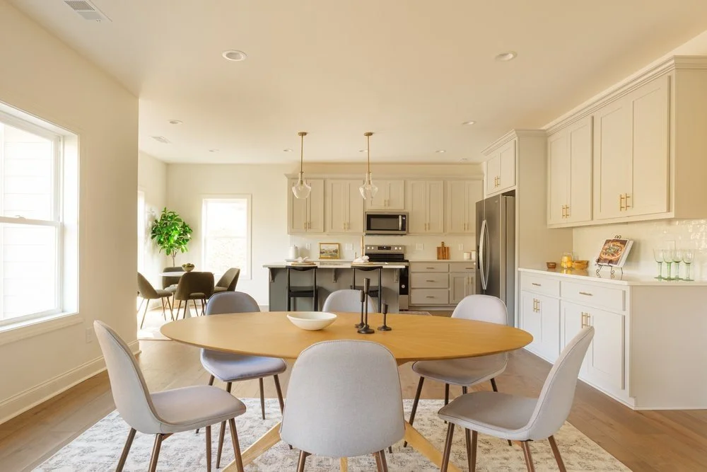 Open concept living in mountain home with modern oval dining table and custom kitchen and breakfast nook in background.