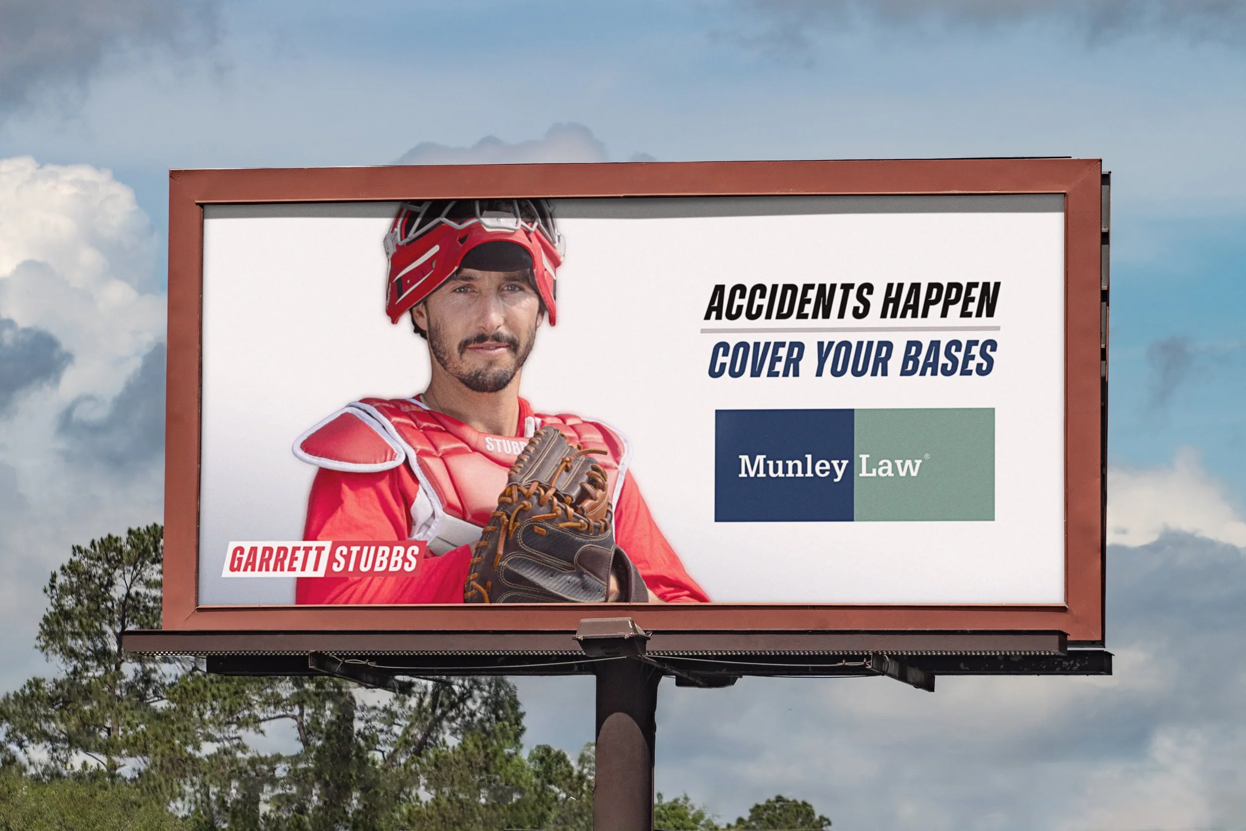 A baseball billboard featuring a man in red catcher's gear and helmet, with text saying 'Accidents happen, cover your bases' and the Munley Law logo. The man's name is Garrett Stubbs.