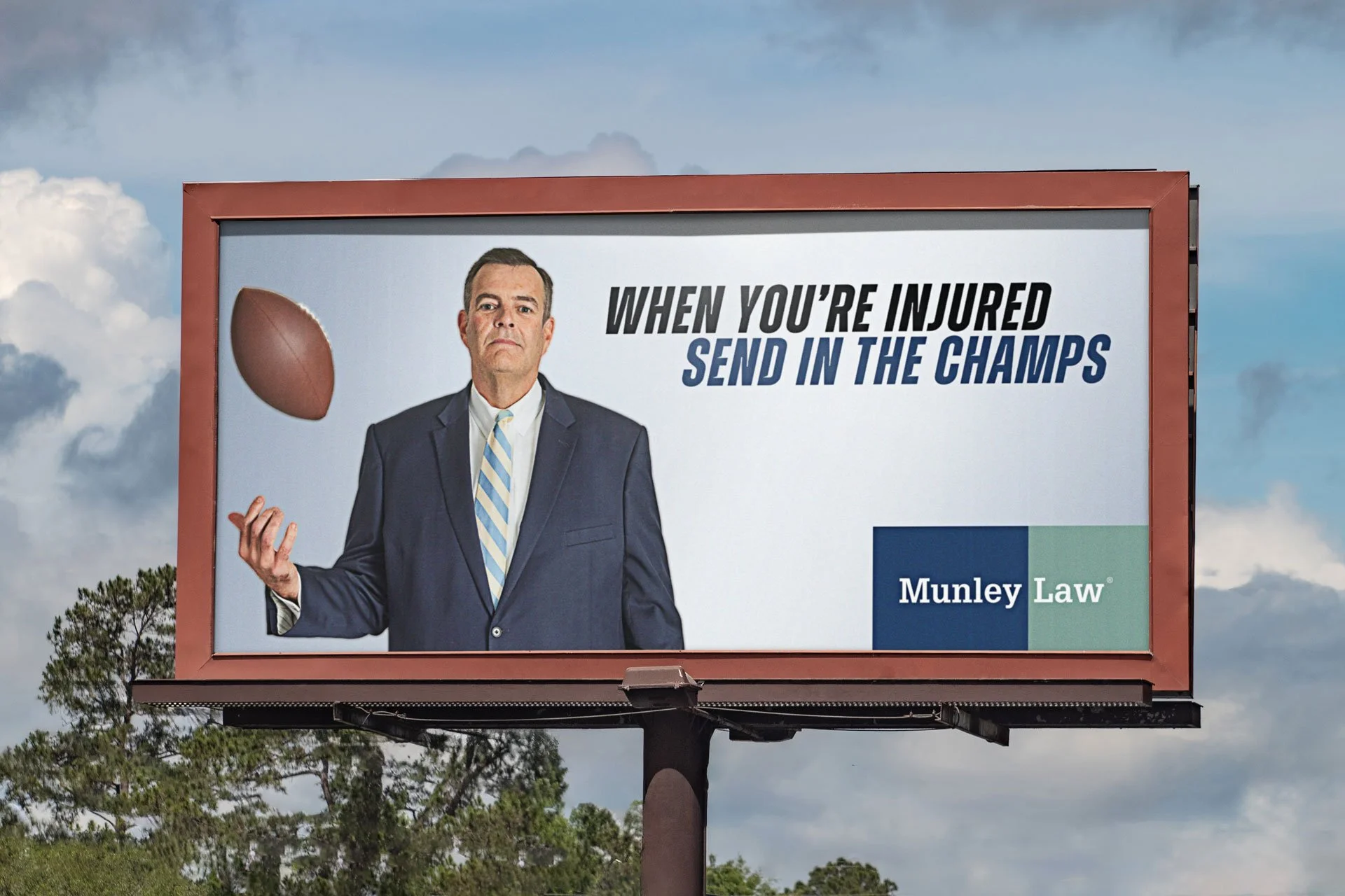 Billboard featuring a man in a suit tossing an American football, with the text 'When you're injured send in the champs' and the logo 'Munley Law'.